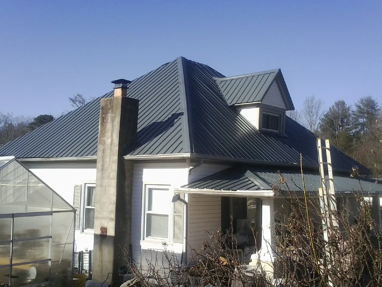 Dark blue standing seam metal roof on a white farmhouse with dormer — Slate & Tile Roof Repair by Roofing Brothers in Campaign