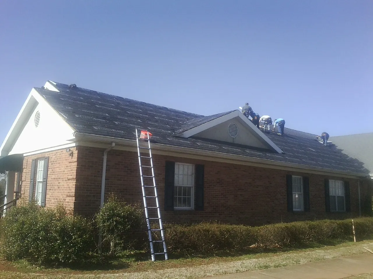Crew tearing shingles off a brick ranch roof with a ladder set — Emergency Roof Repair work by our crew in Campaign