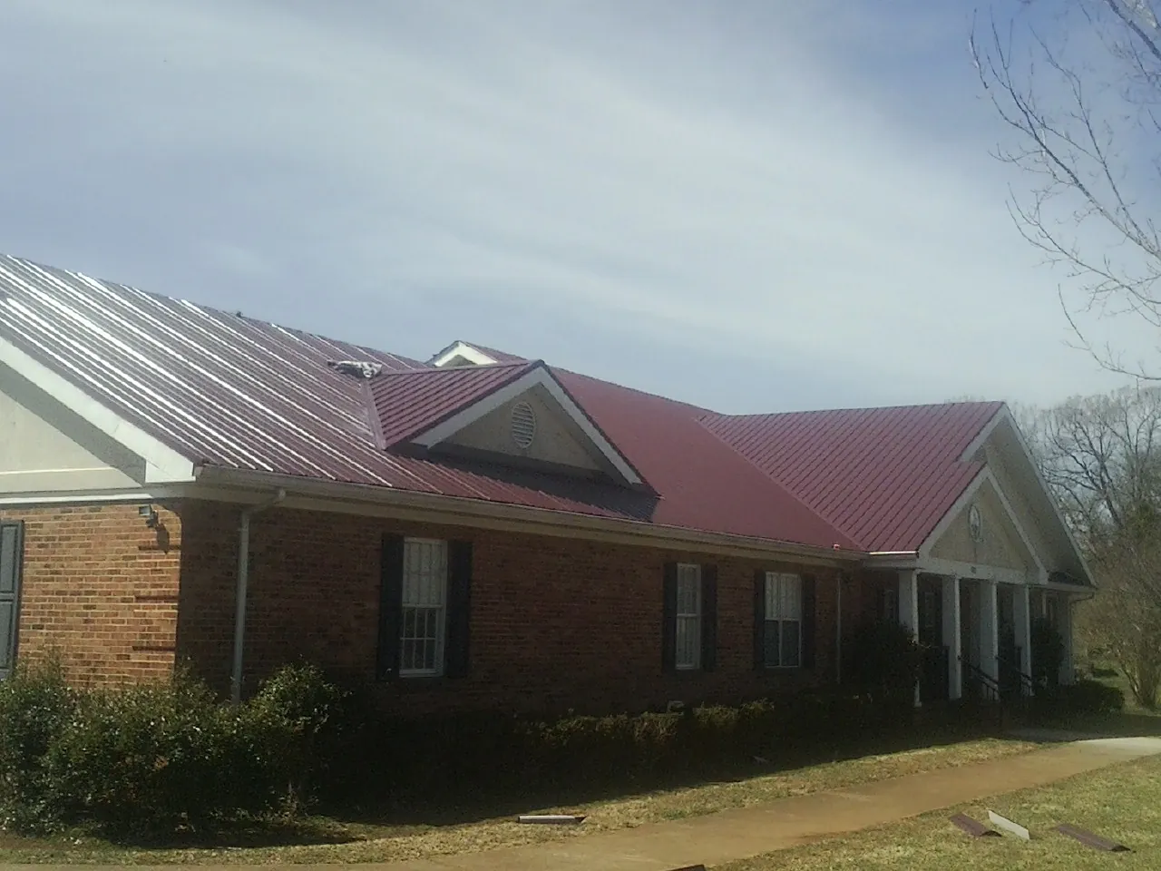 Red metal roof with gabled entries on a long brick building, from a Hail Damage Roof Repair job in Campaign