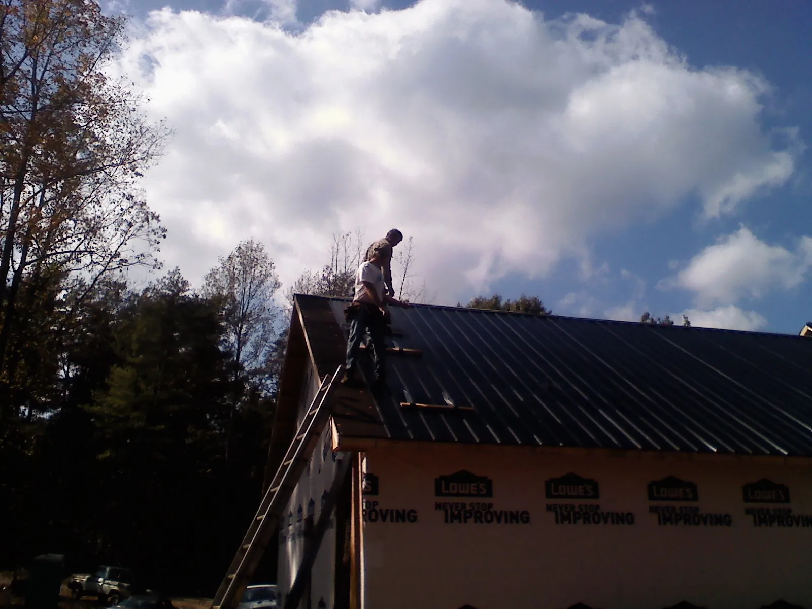 Roofer fastening dark metal panels high against a cloudy sky, from a Roof Inspection job in Campaign