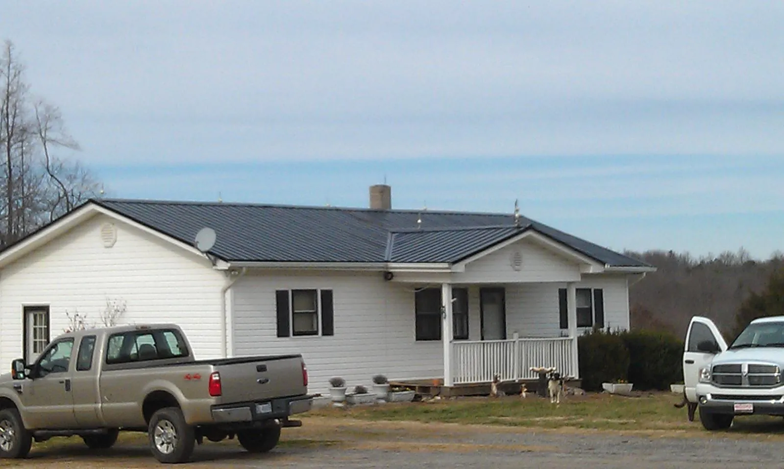 Finished dark metal roof on a white ranch home with work trucks parked in Campaign