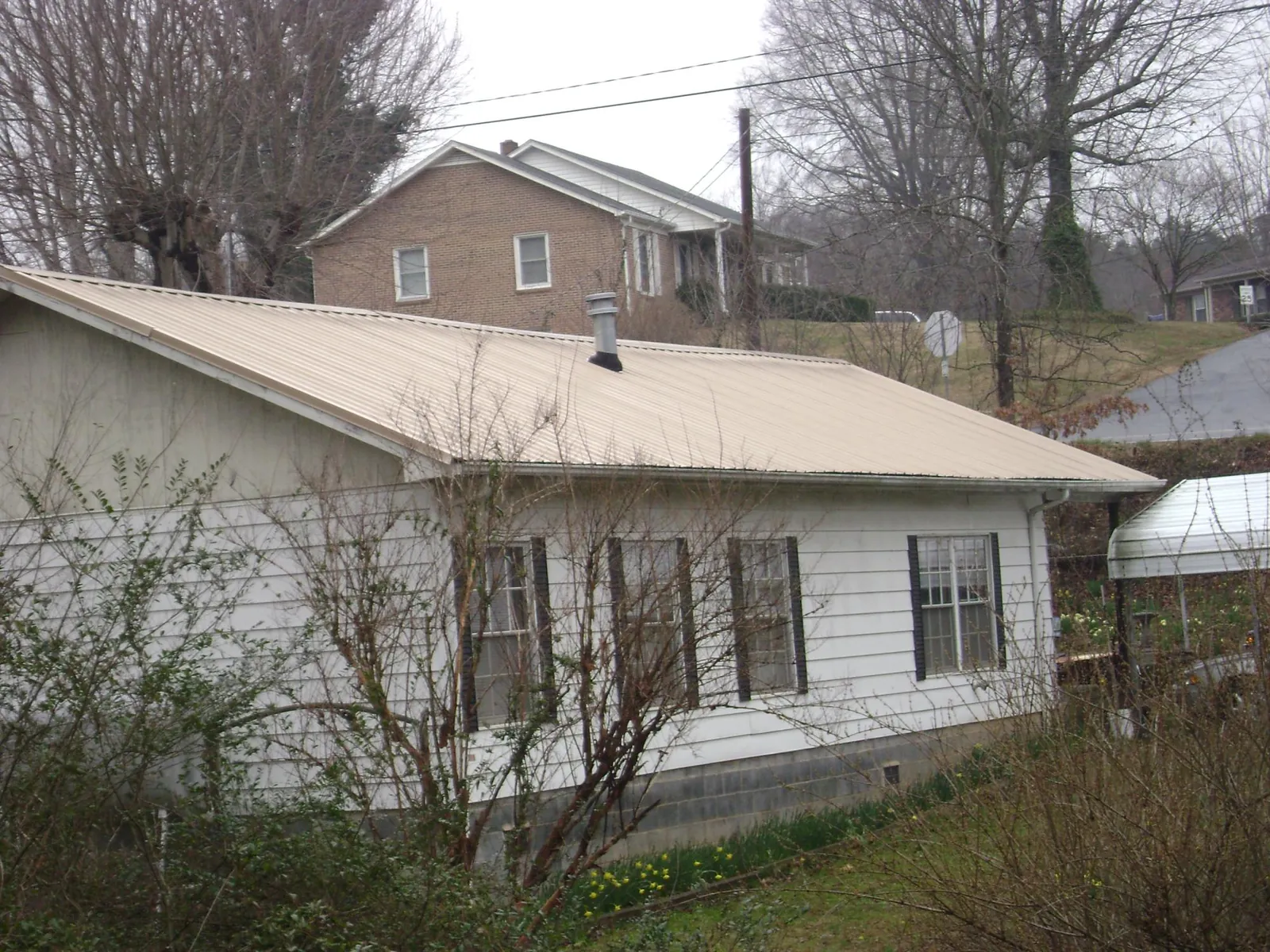 Tan metal roof on a white sided house set into a hillside — Commercial Roofing by Roofing Brothers in Campaign