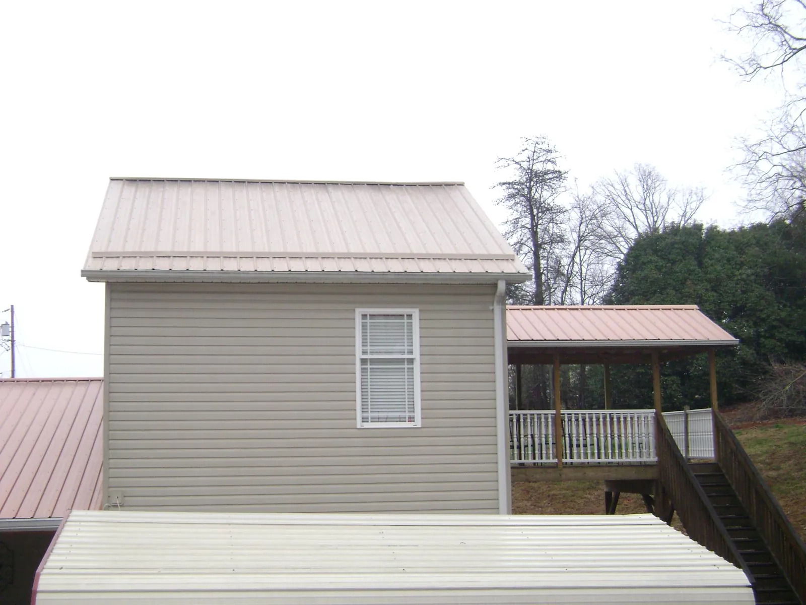 Tan metal roofs on a two story addition and attached porch, from a Roof Replacement job in Campaign